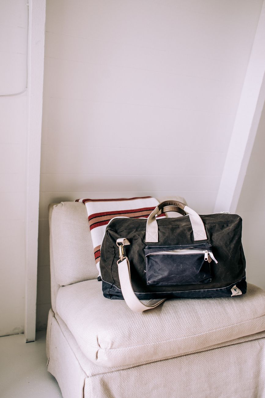 Canvas duffel bag, notebook, and quality clothing laid flat on wood floor